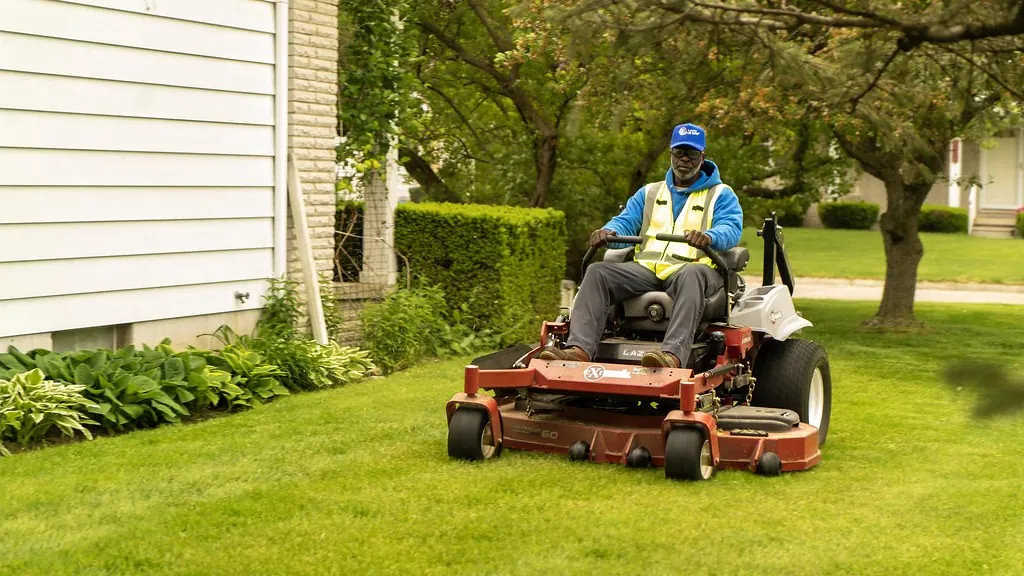 Landscaper riding a zero-turn mower across a front lawn
