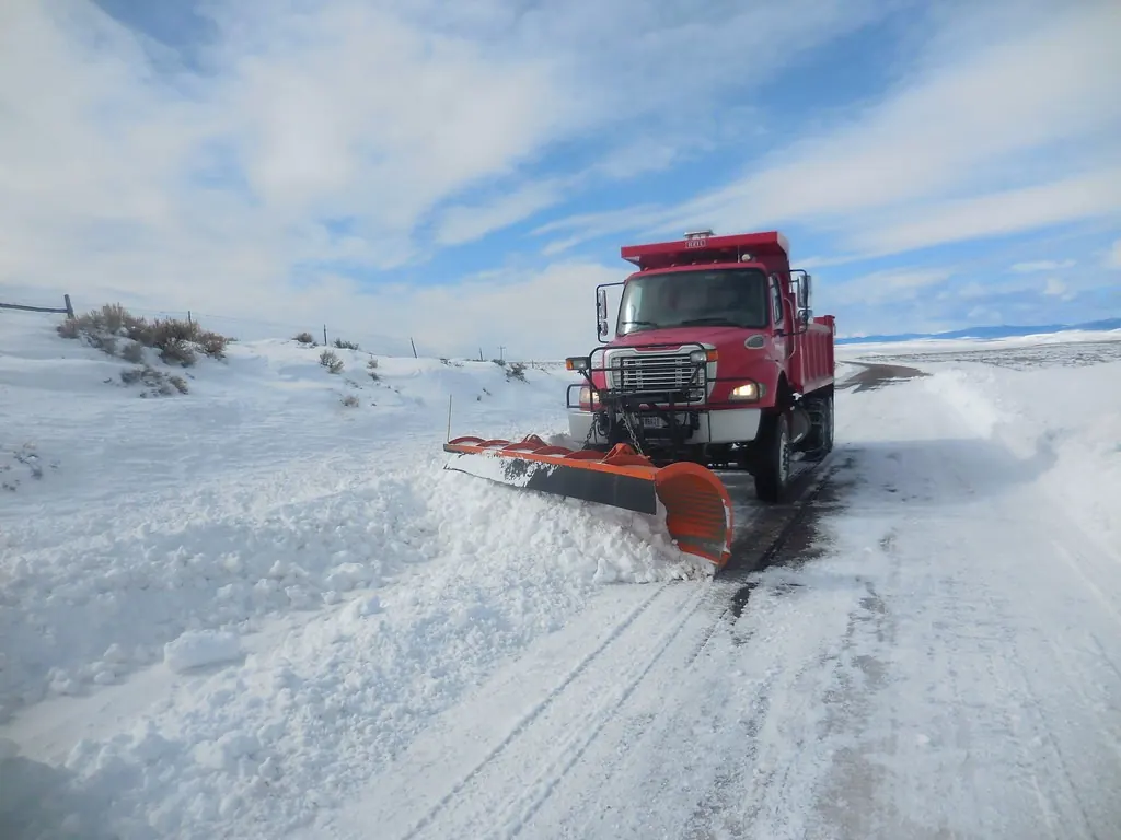Red plow truck clearing a snow-covered road