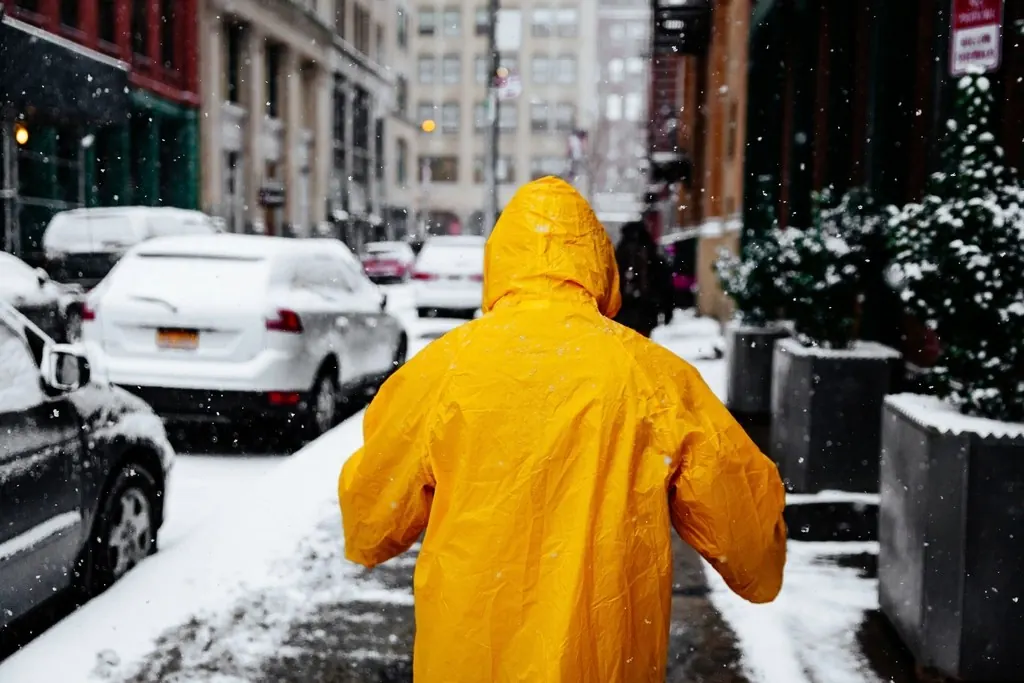 Worker in a yellow raincoat shoveling a city sidewalk