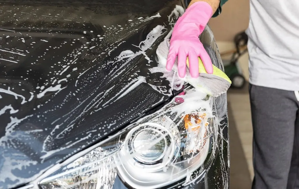 Gloved hand washing a car headlight with foam